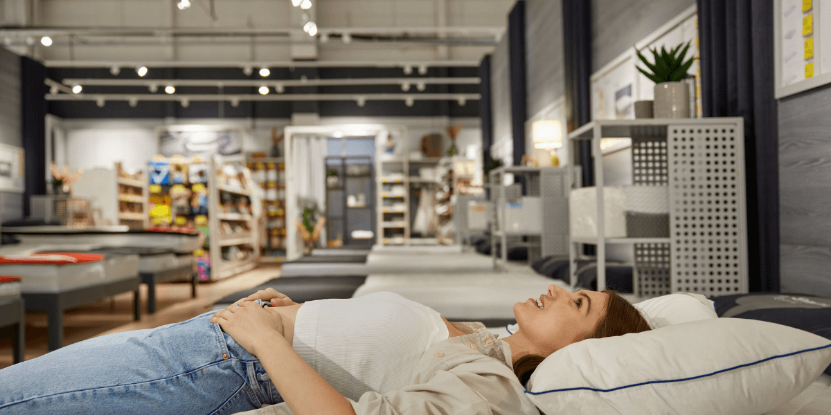 A woman reclines on a bed in a store, showcasing the bedding and mattress for potential customers.